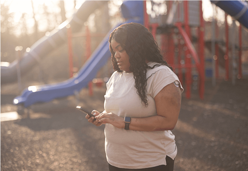 Person using smartphone, standing in a playground with colorful slides, and illuminated by soft, warm sunlight.